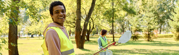 Diverse couple in a bright yellow vests cleaning in a park.