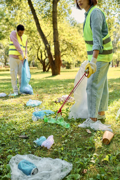 A socially active diverse loving couple in safety vests and gloves clean the park together under the golden sun.