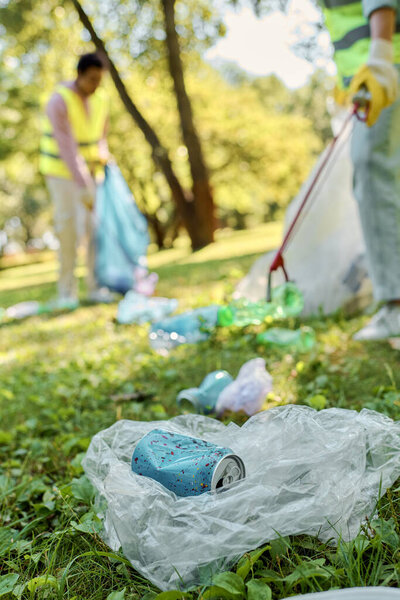 Группа социально активных людей, одетых в спасательные жилеты и перчатки, стоящих вокруг поля, убирающих парк вместе.