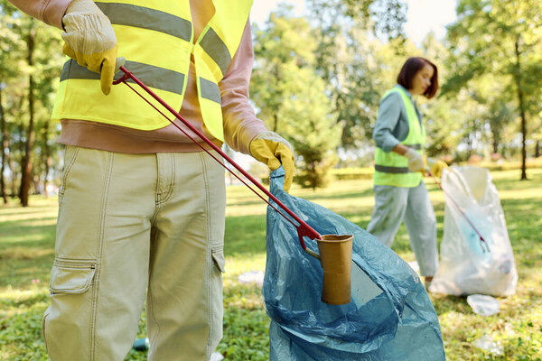A diverse couple in safety vests and gloves cleaning a lush park, embodying environmental stewardship and unity.