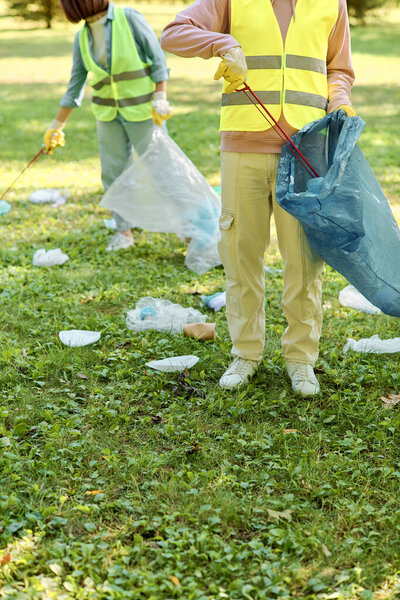 A socially active and loving couple, wearing safety vests and gloves, stand together in the grass cleaning the park.
