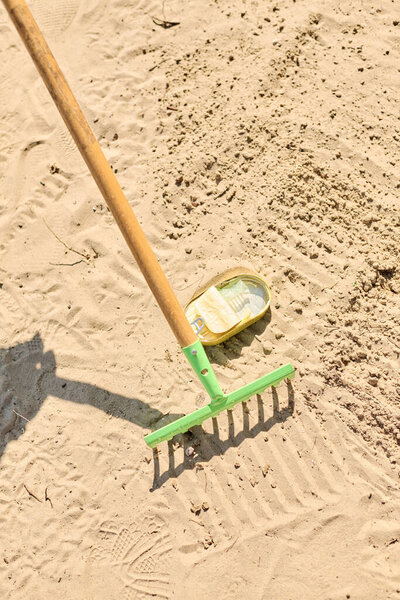A shovel and a rake are peacefully resting on the sandy ground under the sun.