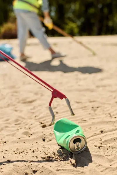 stock image A green can with a red handle sits on a sandy beach, symbolizing environmental stewardship and beach cleaning efforts.