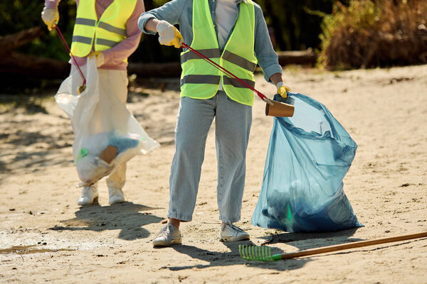 A couple in safety vests and gloves stands in the sand, united in cleaning a park together.