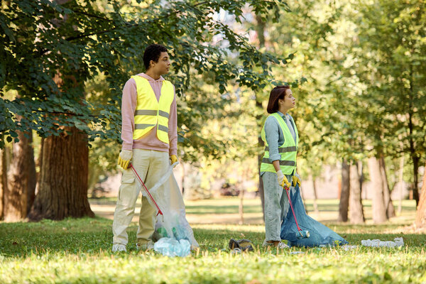 A socially active, diverse couple in safety vests and gloves cleaning the park together.
