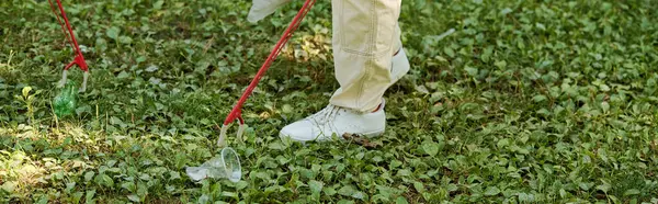 Bir insan çimlerin üzerinde durur, çimlerden plastik bardakları temizler.