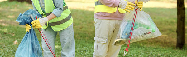 Два человека в защитных жилетах и перчатках стоят в траве, проявляя любовь и заботу об окружающей среде парка.