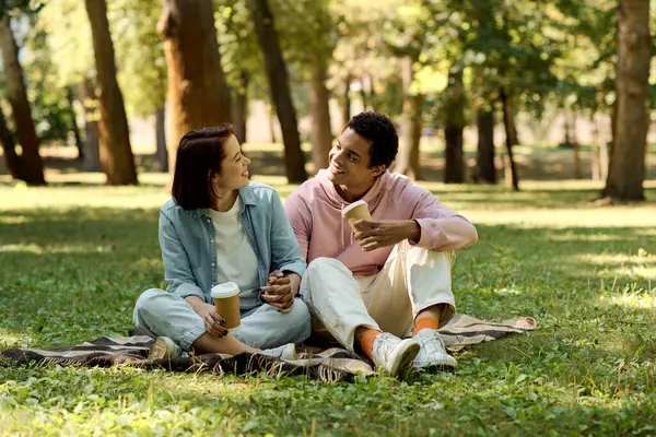 stock image A diverse couple in vibrant attire enjoying a leisurely afternoon on a blanket in a park.