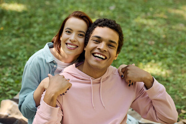 Мужчина и женщина, одетые ярко, сидят на одеяле в пышной зеленой траве, наслаждаясь расслабляющим моментом вместе.