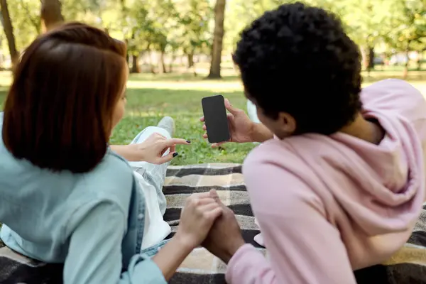 stock image A diverse loving couple in vibrant attires looking at phone, enjoying each others company.