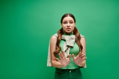 20 'li yaşlarda korkmuş genç bir kadın canlı yeşil bir arka planın önünde duruyor..