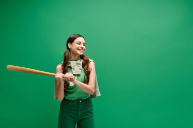 A young beautiful woman in her 20s holding a baseball bat in front of a vibrant green background. clipart