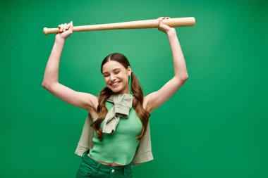A young, beautiful woman in her 20s poses in a studio setting, defiantly holding a baseball bat over her head. clipart