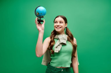 20 'li yaşlarda genç ve güzel bir kadın yeşil bir stüdyoda büyüleyici bir mavi küreyi nazikçe tutuyor..