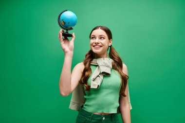 A young beautiful woman in her 20s is delicately holding a mesmerizing blue globe in a studio setting on green. clipart