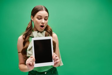 20 'li yaşlarda genç bir kadın yeşilde yüzünün önünde bir tablet tutuyor.