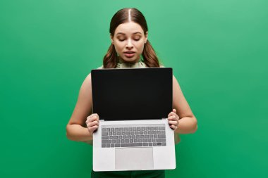 20 'li yaşlarda genç bir kadın bir stüdyo ortamında kimliğini gizleyen bir dizüstü bilgisayar tutuyor..