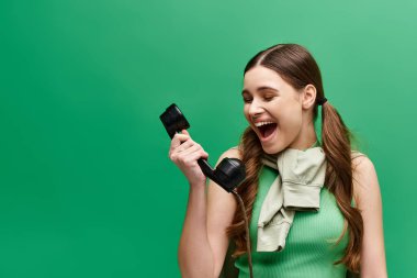 20 'li yaşlarda genç bir kadın stüdyo ortamında eski moda bir telefonu yüzüne tutarak nostaljik bir görünüm sergiliyor..