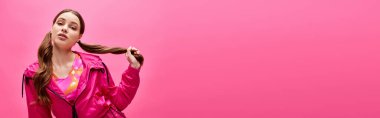 20 'li yaşlarda, uzun saçlı, pembe elbiseli şık bir kadın stüdyoda pembe bir arka plana karşı poz veriyor..