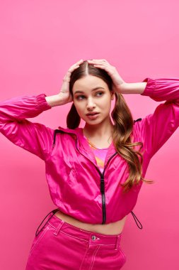 20 'li yaşlarda şık bir kız pembe ceketli ve pantolonlu pembe arka planlı bir stüdyoda..