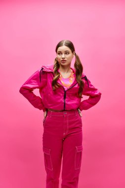 20 'li yaşlarda şık bir kız pembe bir tulumla canlı pembe bir arka plana karşı güvenle duruyor..