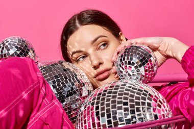 A stylish young woman in her 20s, dressed in a pink outfit, holds a reflective mirror ball in a vibrant studio setting. clipart