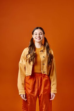 20 'li yaşlarda şık bir kadın canlı turuncu bir arka planda, stüdyo ortamında güvenle ayakta duruyor..