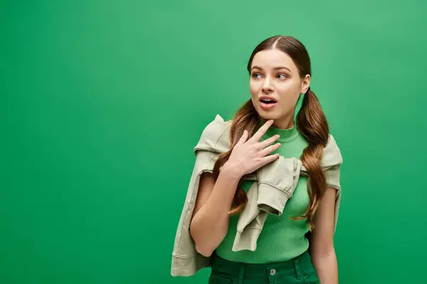 stock image A young woman in her 20s in a green shirt holds her hands peacefully on her chest in a studio setting.