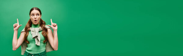 A young woman in her 20s holds two fingers up in front of her face in a studio setting on green.