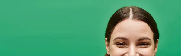 stock image A young woman in her 20s smiles warmly against a vibrant green background in a studio setting.
