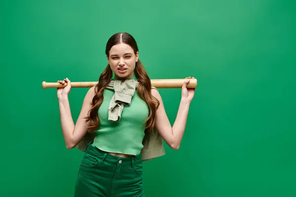 一位20多岁的年轻漂亮女子背着棒球棒站在工作室里 背景是绿色的 — 图库照片
