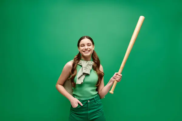 20代の若い女性は自信を持って 印象的な緑の背景に対して野球バットを保持しています — ストック写真