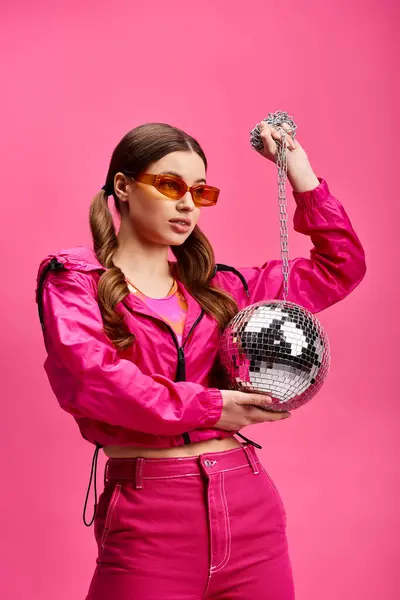 ピンクの服を着た20代のスタイリッシュな若い女性は ピンクの背景を持つスタジオでディスコボールを保持しています — ストック写真