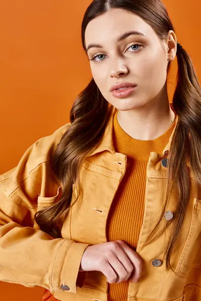 一位20多岁的时髦女人 一头长发 穿着一件黄色夹克 衬托着橙色的背景 — 图库照片