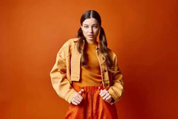 一位20多岁的年轻而时尚的女人自信地站在工作室里明亮的橙色背景前 — 图库照片