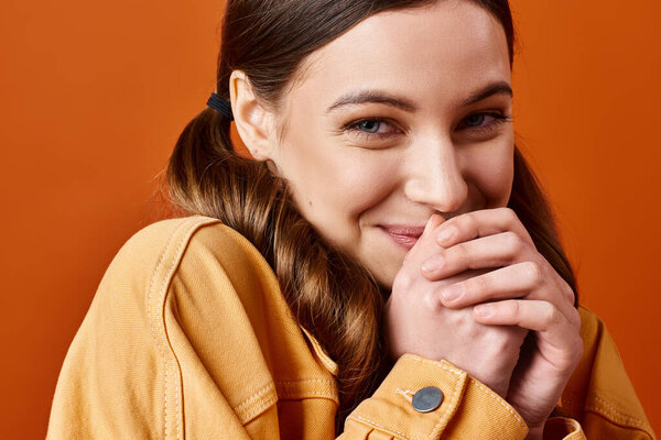 A young, stylish woman in her 20s, exuding joy and confidence, smiles brightly with her hands gracefully resting on her chin.
