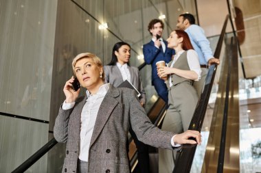 Hareket halindeki bir yürüyen merdivende dururken cep telefonuyla konuşan bir iş kadını..