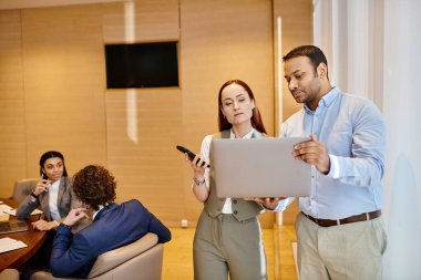 Diverse business professionals collaborate around a table with a laptop. clipart