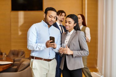 A man and woman of different ethnicities engrossed in a cell phone together. clipart