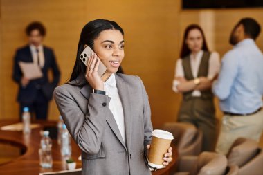 Bir kadın sohbet ederken bir cep telefonu ve bir fincan kahveyi zarifçe dengeler..