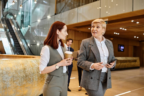 Two women of different races engaged in conversation in a lobby.