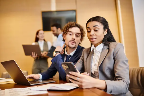 stock image Man and woman of different ethnicities sitting at a table, engrossed in a cell phone screen.