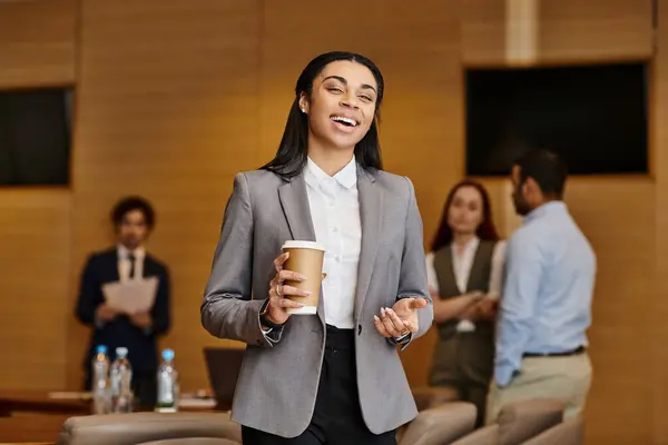 stock image A woman of color enjoying a cup of coffee in a diverse business meeting room.