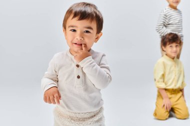 Küçük bir çocuk omuzlarında oturan küçük bir çocuğu destekliyor, ikisi de gri bir geçmişi olan bir stüdyoda neşeli bir şekilde gülümsüyor..