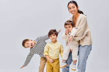 Asian mother gracefully poses with her children in a studio against a grey backdrop, glowing with love and joy. clipart