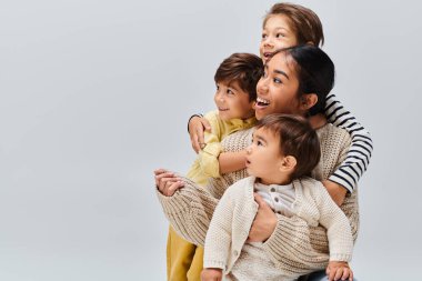 A group of children, including a young Asian mother, stack on top of each other in a playful and creative tower formation. clipart