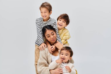 Genç bir Asyalı anne ve çocukları, bir stüdyoda gri bir zemine karşı sevgi ve beraberlik içinde poz veriyorlar..