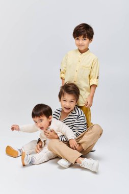 A trio of children, seated on the floor, engage in playful interaction with one another in a cozy studio setting. clipart