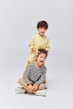 Two young boys, sitting on the ground, are in awe with their mouths wide open in a studio setting clipart