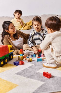 Genç bir Asyalı anne, küçük oğullarıyla evlerinin oturma odasının zemininde oynayarak mutlu oluyor..